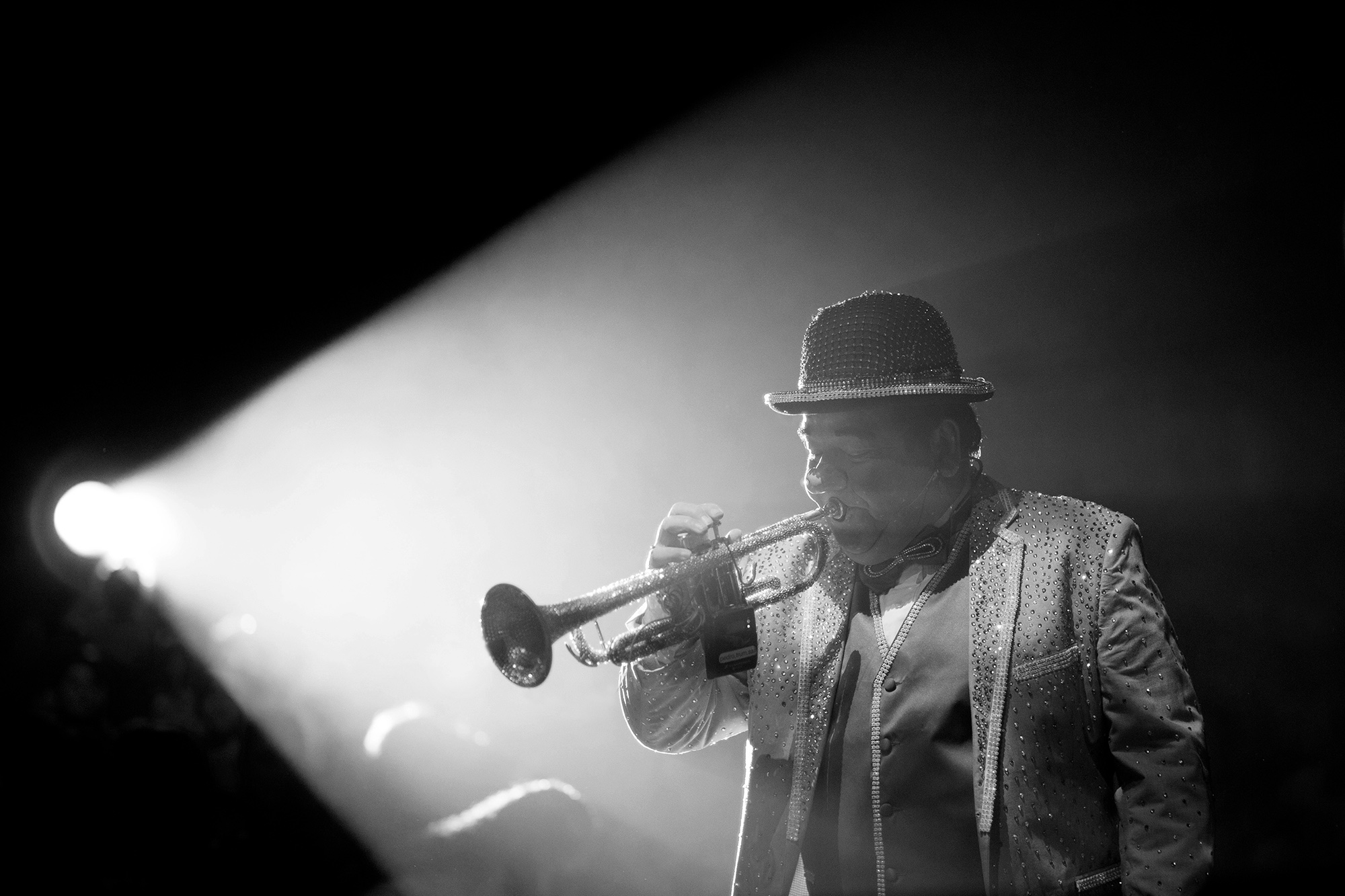 Black and white photograph of a circus trumpet player in spotlight.